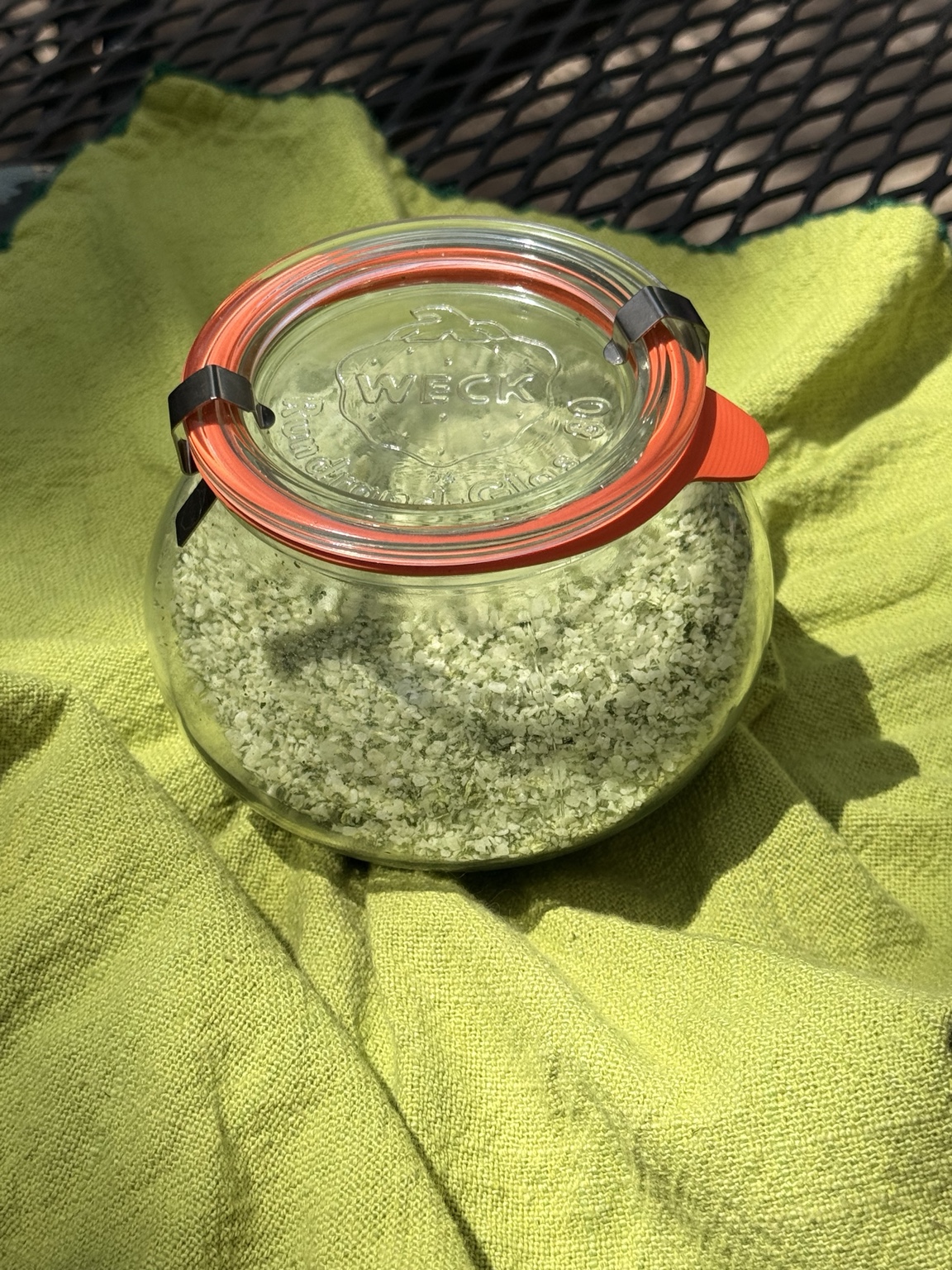 Homemade basil salt in a glass jar on a chartreuse linen