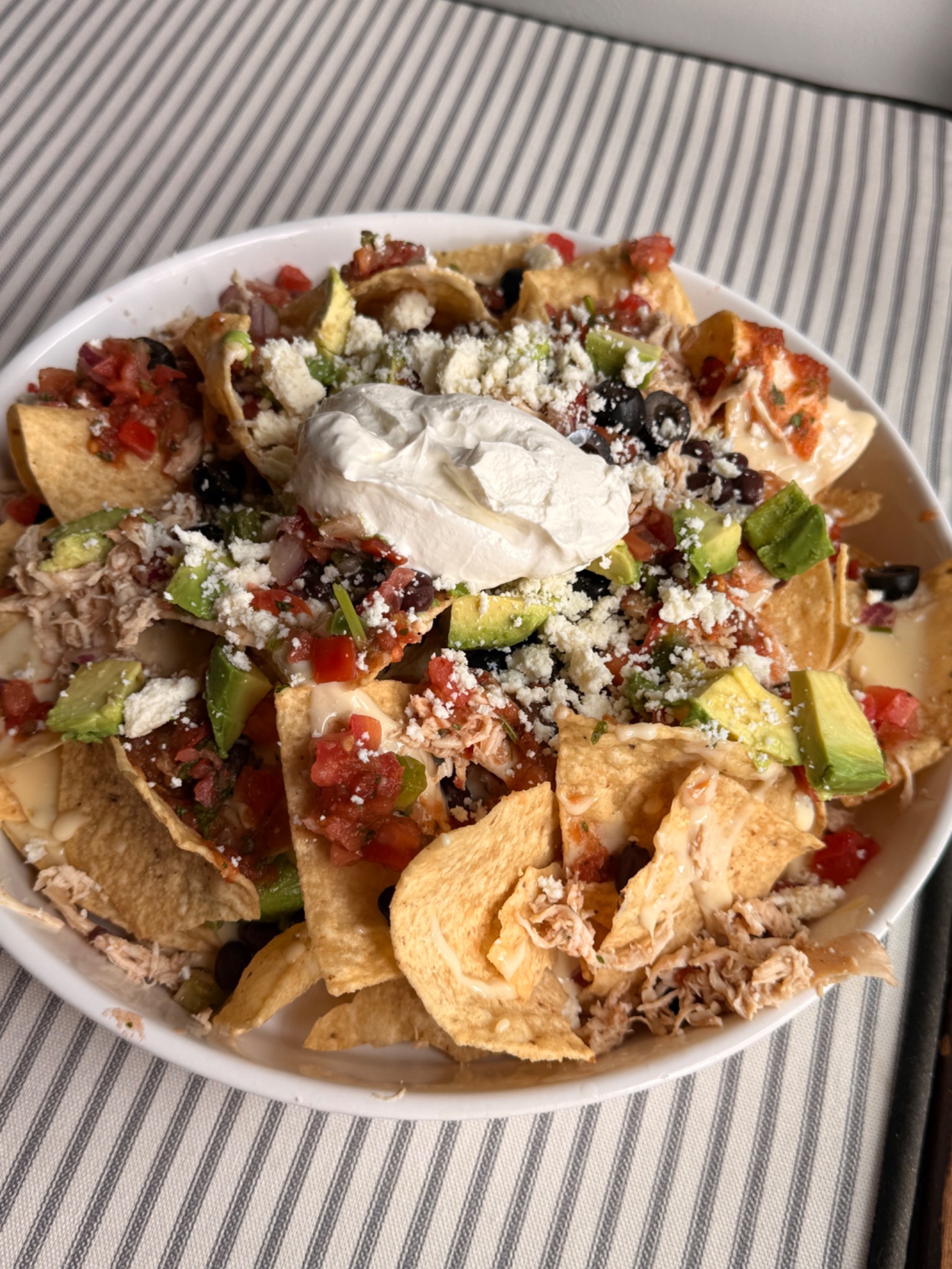 Ultimate nachos layered with shredded chicken, white queso, black beans, pico de gallo, avocado, olives, queso fresco and sour cream
